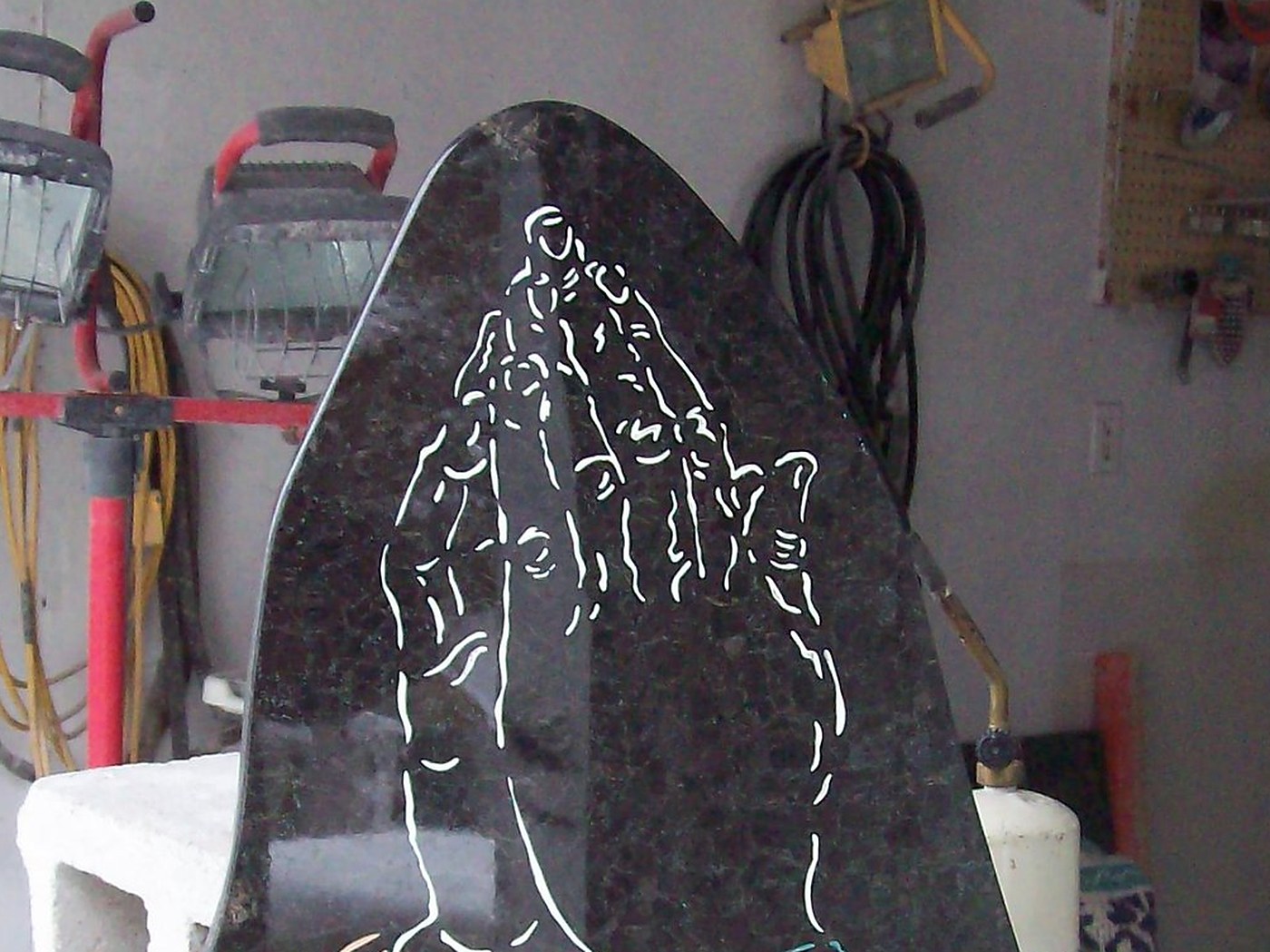 A granite memorial cut to a pointed arch, with praying hands engraved into the face