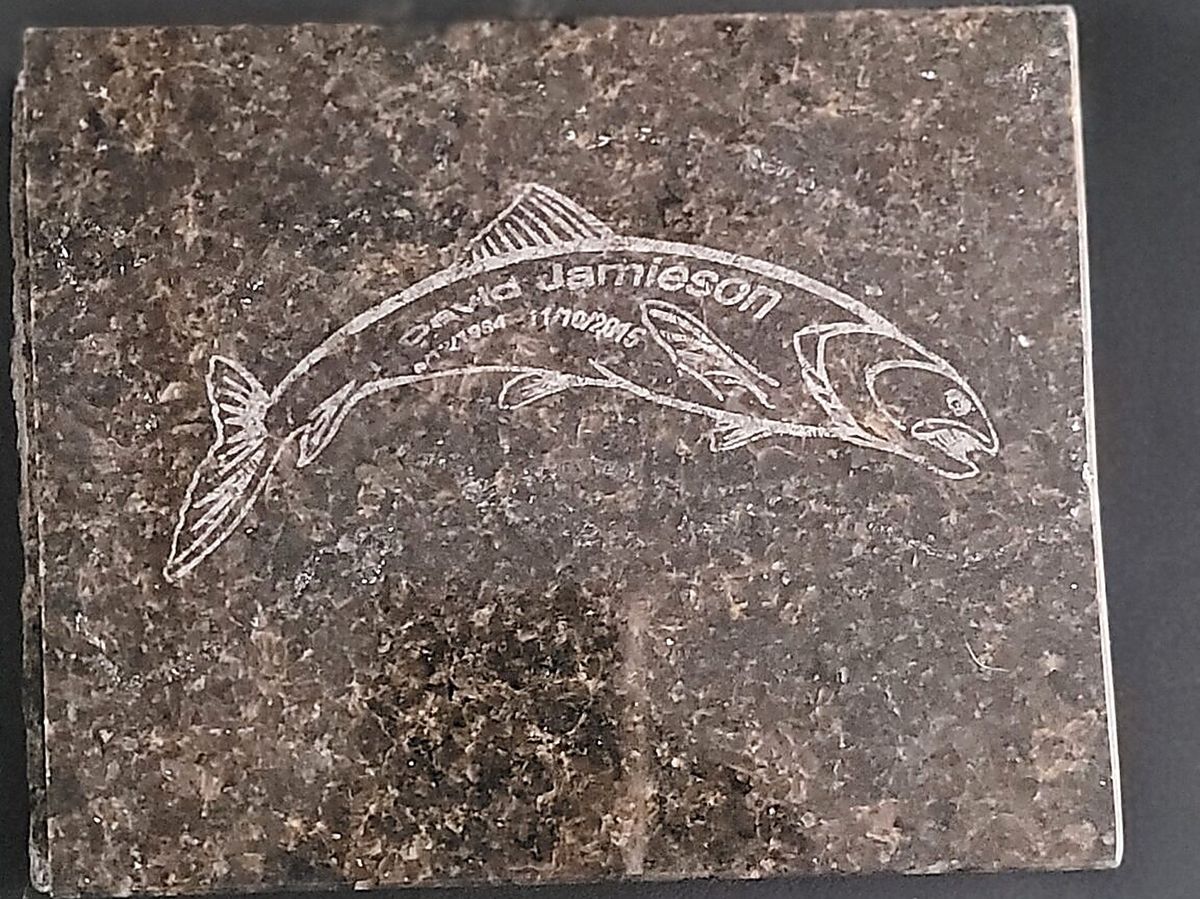 A salmon engraved into a polished granite slab, with a name and two dates