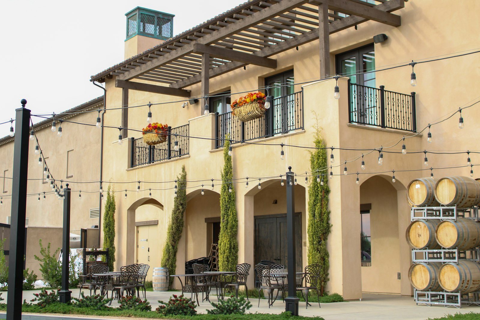 An empty winery courtyard with tables, string lights and stacked oak barrels
